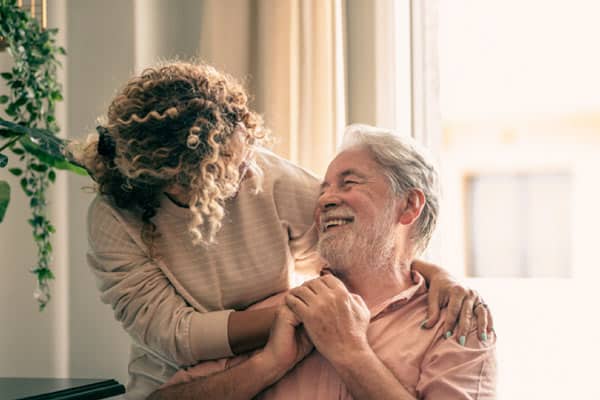 Image alt text: A woman hugs her elderly father as she helps him with managing chronic illnesses at home.